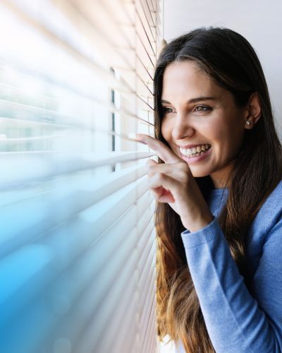 Frau an einem Fenster mit Jalousien